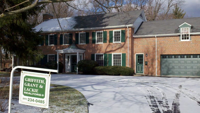 A house with green shutters and snow on the ground.
