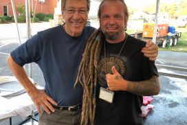 Two men standing under a tent with dreadlocks.