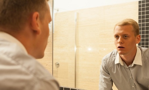 A man in the bathroom looking at himself in the mirror