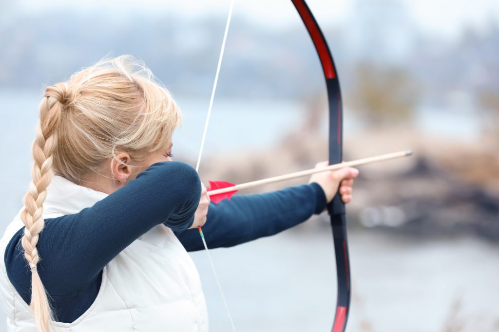 A woman is aiming at a target with a bow and arrow.