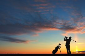 A person standing on top of a hill holding onto a golf bag.