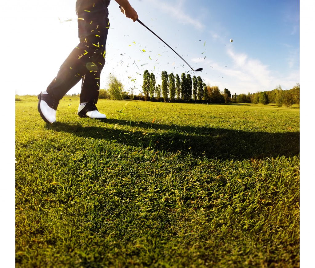 A man is hitting a golf ball on a green field.